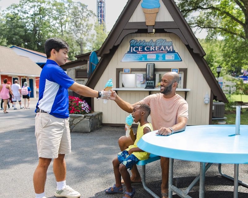A Team Member handing a young boy and father an Udderly Blue Ice Cream cone.